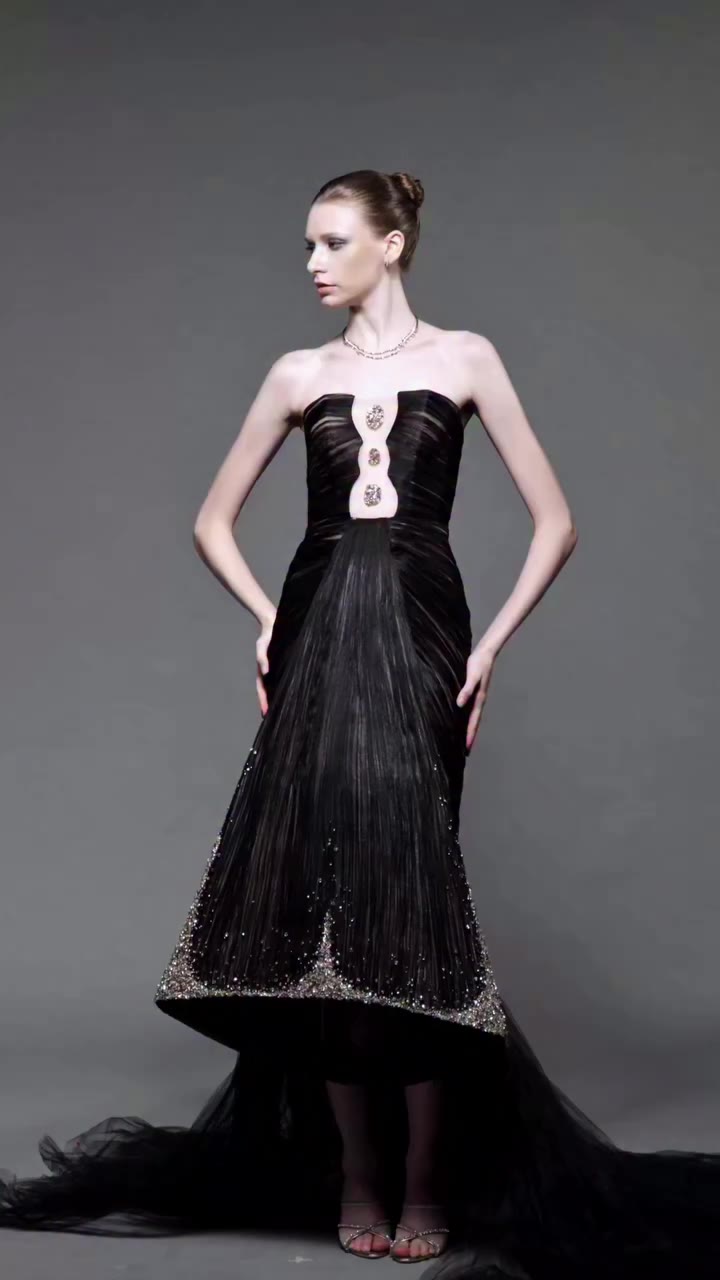 A sculptural black strapless mermaid gown defined by a dramatic keyhole…
