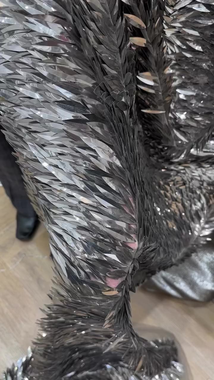 Intricately layered metallic embellishments create a striking, feather-like…